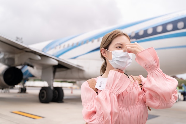 Aziatische vrouw die beschermend gezichtsmasker draagt bij vliegtuig