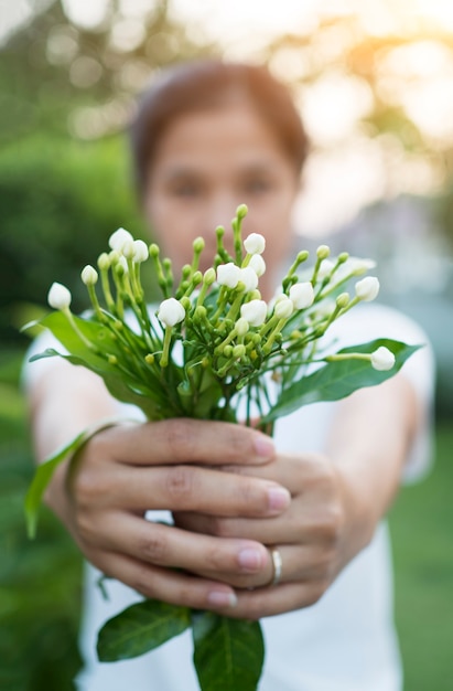 Aziatische vrouw die bloemen in tuin hokding.