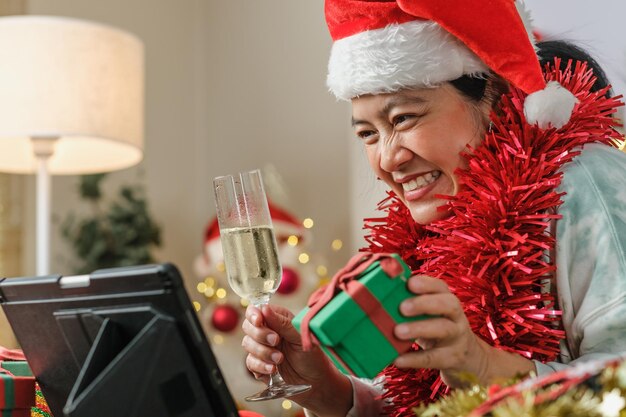 Aziatische vrouw die champagne roostert, viert nieuwjaar en kerstfeest video-oproep vrienden thuis