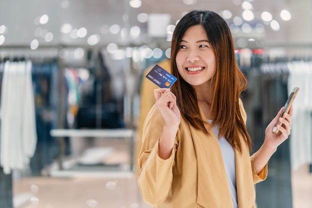 Aziatische vrouw die creditcard met mobiele telefoon voor online het winkelen in warenhuis met behulp van