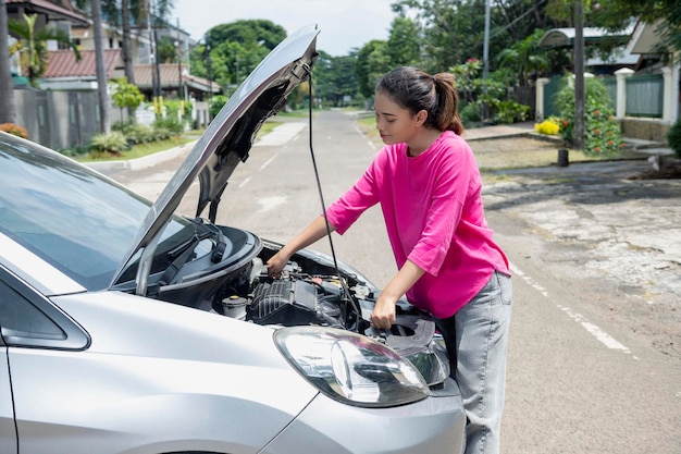 Aziatische vrouw die de motorkap opent en op zoek gaat naar problemen, de auto gaat kapot