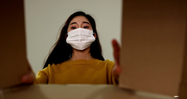 Aziatische vrouw die een beschermend gezichtsmasker draagt, bereidt de pakketdoos voor en verpakt deze voor levering aan de klant