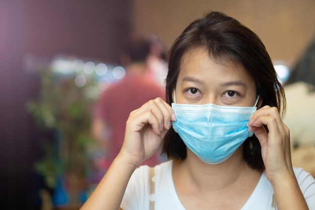 Aziatische vrouw die een beschermend masker op haar gezicht draagt terwijl ze in de coffeeshop is tijdens de pandemie van het virus COVID-19.