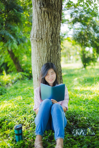 Aziatische vrouw die een boek in het park leest, Aziatisch meisje dat een boek leest in het park onder de zonsondergang