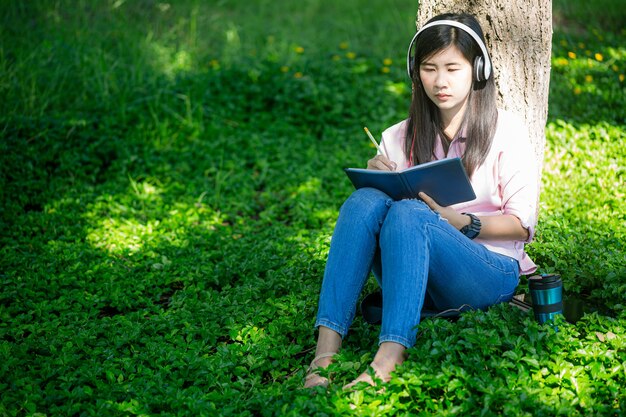 Aziatische vrouw die een boek leest en in het park glimlacht Tevreden aziatische vrouw die een boek in een park leest