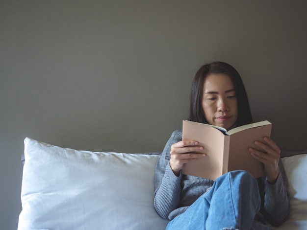 Aziatische vrouw die een boek op de stoel leest