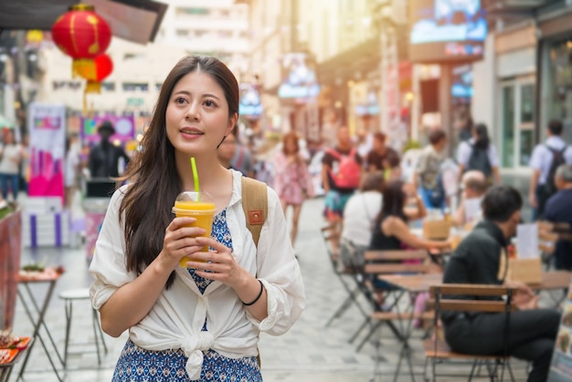 Aziatische vrouw die een kopje mangosap vasthoudt en tegelijkertijd op de straatmarkt loopt om op de markt te winkelen.