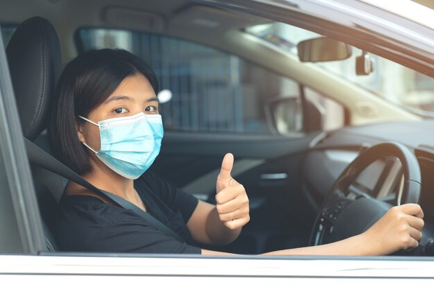 Aziatische vrouw die een masker draagt dat in de auto zit om coronavirus te voorkomen