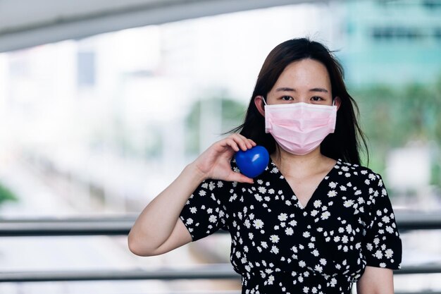 Aziatische vrouw die een masker draagt en een blauw hart bij de hand houdt ter bescherming van het Coronavirus- of COVID19-concept