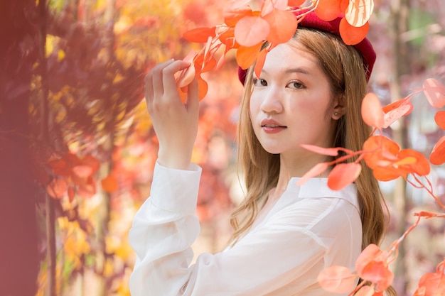 Aziatische vrouw die een wit overhemd en een rode muts draagt, staat in roodoranje bladeren als bos in de herfst.