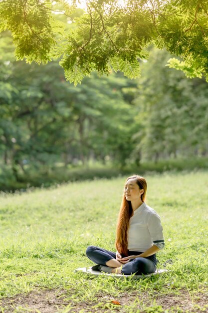 Aziatische vrouw die een witte kledingsmeditatie in het park draagt bij zonsopgang in de lente of de zomer