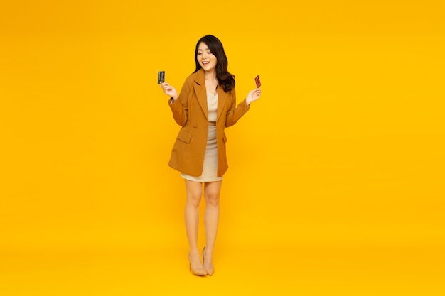Aziatische vrouw die en creditcard glimlacht toont op gele muur.