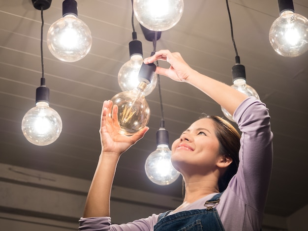 Aziatische vrouw die gloeilamp verandert