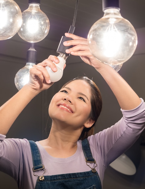 Aziatische vrouw die gloeilamp verandert