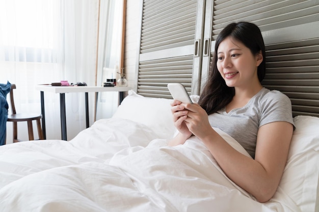 Aziatische vrouw die in bed ligt en haar mobiel sms't naar haar minnaar en lief lacht.