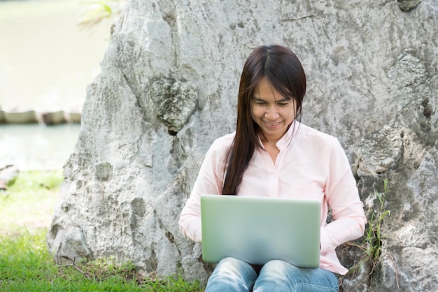 Aziatische vrouw die in een groen park zit met een laptopcomputer vrouw die op een laptop werkt, gelukkige ondernemer