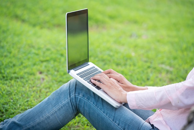 Aziatische vrouw die in het groene park zit met behulp van een laptopcomputer vrouw die op een groene laptop in het park werkt