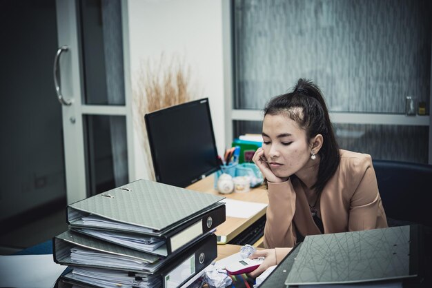 Aziatische vrouw die in kantoor werkt Jonge zakenvrouw gestrest door overbelasting van het werk met veel dossier op het bureau