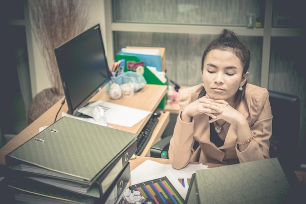Aziatische vrouw die in kantoor werkt Jonge zakenvrouw gestrest door overbelasting van het werk met veel dossier op het bureau