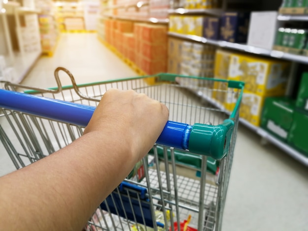 Aziatische vrouw die in supermarktopslag winkelt met duwend boodschappenwagentje