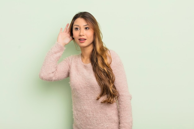 Aziatische vrouw die lacht en nieuwsgierig naar de zijkant kijkt, probeert te luisteren naar roddels of een geheim af te luisteren