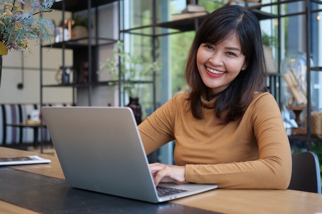 Aziatische vrouw die laptop computer in de koffie van de koffiewinkel met behulp van