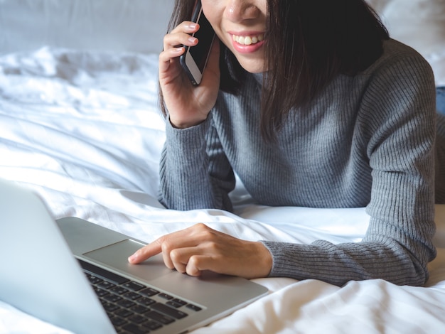 Aziatische vrouw die laptop op het bed met behulp van