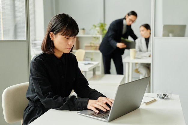 Aziatische vrouw die laptop op kantoor gebruikt