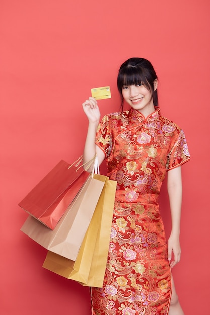 Aziatische vrouw die met Chinese kleding een creditcard en het winkelen zakken houdt