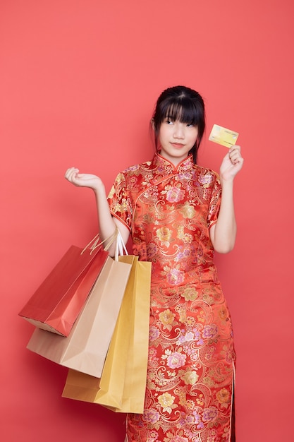 Aziatische vrouw die met Chinese kleding een creditcard en het winkelen zakken houdt