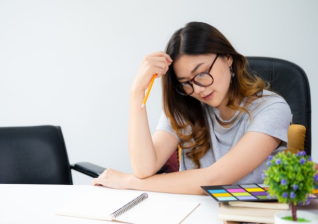 Aziatische vrouw die met lang gouden haar glazen draagt die bij het bureau zitten