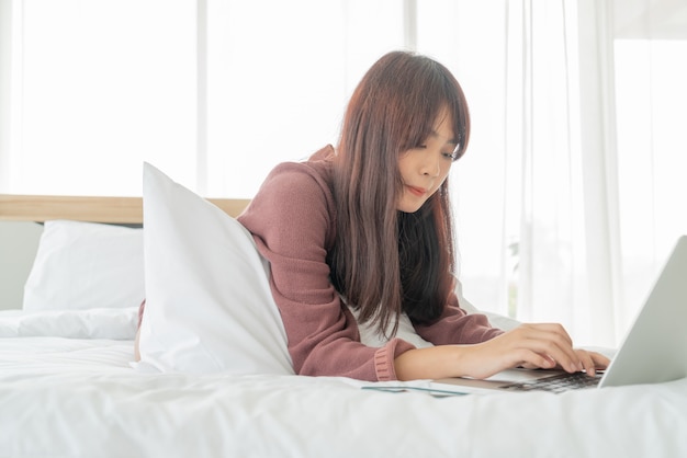 Aziatische vrouw die met laptop aan bed werkt