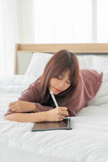 Aziatische vrouw die met tablet op bed werkt