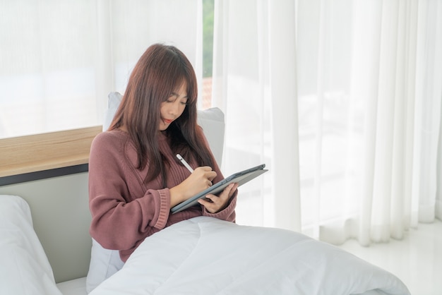 Aziatische vrouw die met tablet op bed werkt