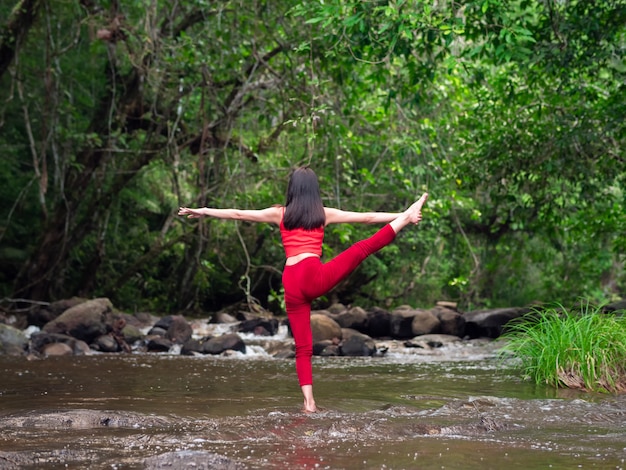 Aziatische vrouw die of yoga praktizeren doen bij de waterval