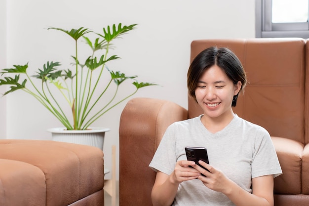 Aziatische vrouw die op een mobiele telefoon zit en gelukkig thuis glimlacht