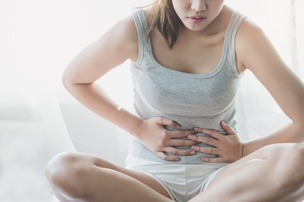 Aziatische vrouw die op het bed legt dat aan buikpijn lijdt. vrouw die lijdt aan menstruatie