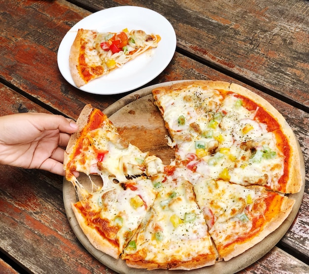 Foto aziatische vrouw die pizza in een dienblad met de hand plukken die in stukken op een houten lijst wordt verdeeld