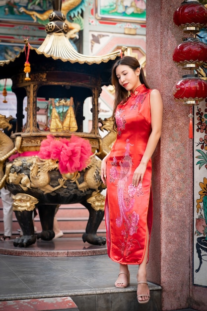 Aziatische vrouw die rode kleding Cheongsam draagt bij Chinees heiligdom. Chinees Nieuwjaar concept.