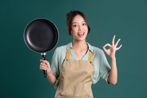 Aziatische vrouw die schort draagt en een pan houdt