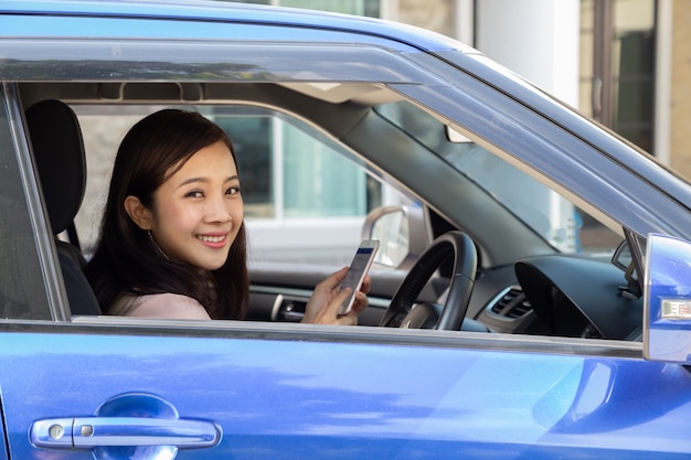 Aziatische vrouw die slimme telefoon in een auto op de weg met behulp van