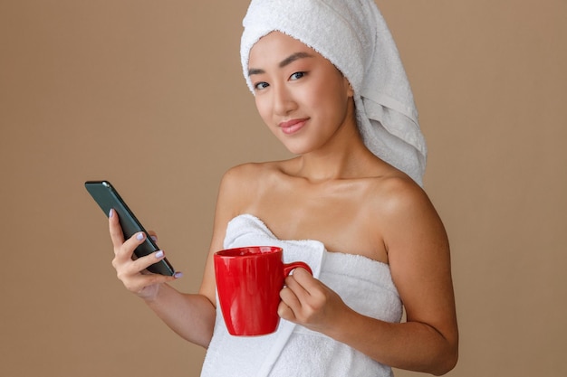 Aziatische vrouw die smartphone gebruikt en koffie drinkt na het douchen