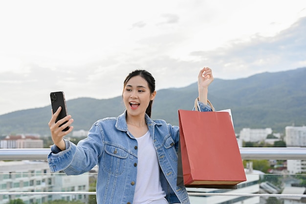 Aziatische vrouw die smartphone gebruikt terwijl ze boodschappentassen draagt