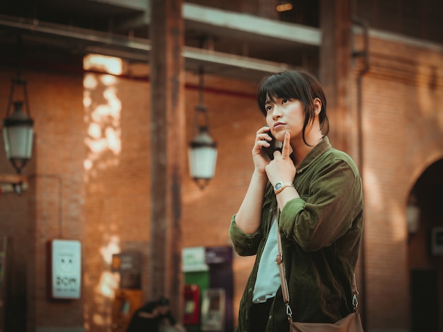 Aziatische vrouw die smartphone met gelukkige stemming in winkelcomplex gebruiken
