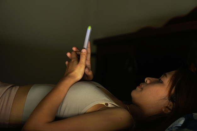 Aziatische vrouw die telefoon op bed gebruikt