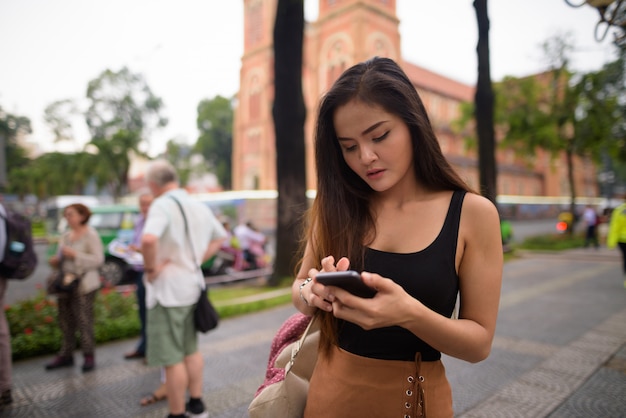 Aziatische vrouw die telefoon voor Notre Dame-Kathedraal in Ho Chi Minh-Stad met behulp van