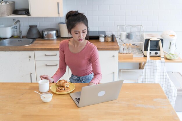 Aziatische vrouw die thuis werkt en eet bij de keuken. Ze werkt thuis.
