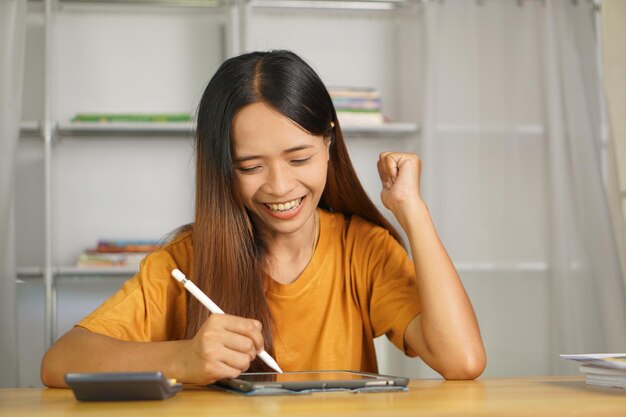 Aziatische vrouw die thuis werkt gelukkig van het kijken naar de winst via de computer