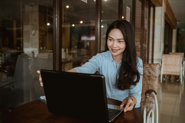 Aziatische vrouw die vrijetijdskleding draagt die met laptop in co-working space werkt