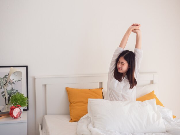 Aziatische vrouw die zich uitstrekt in bed na wakker worden